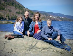 Our family seated on a rock with blue water and a hill in the background