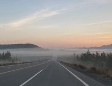 a long road disappearing into fog at the base of mountains
