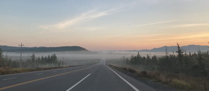 a long road disappearing into fog at the base of mountains